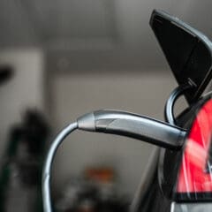 A close-up of EV charging in progress, with a cable plugged into the vehicle’s port and the taillight visible in a garage setting. Ideal for properties needing landlord certificates or electrical rewires.