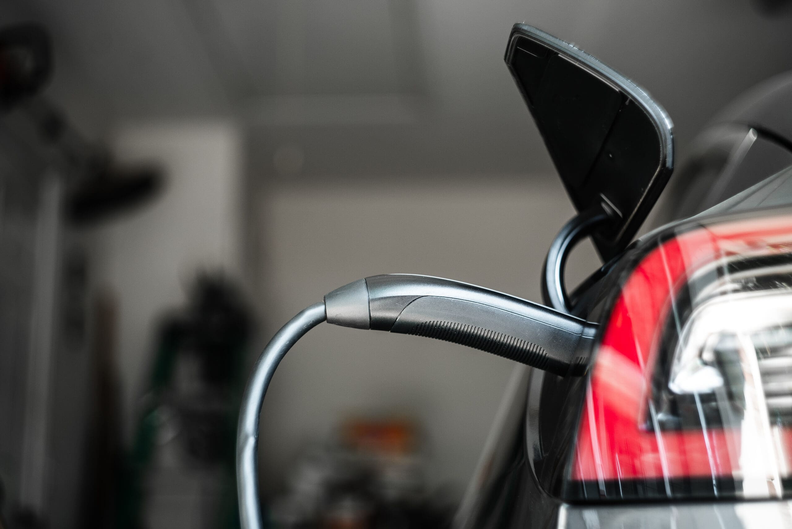 A close-up of EV charging in progress, with a cable plugged into the vehicle’s port and the taillight visible in a garage setting. Ideal for properties needing landlord certificates or electrical rewires.