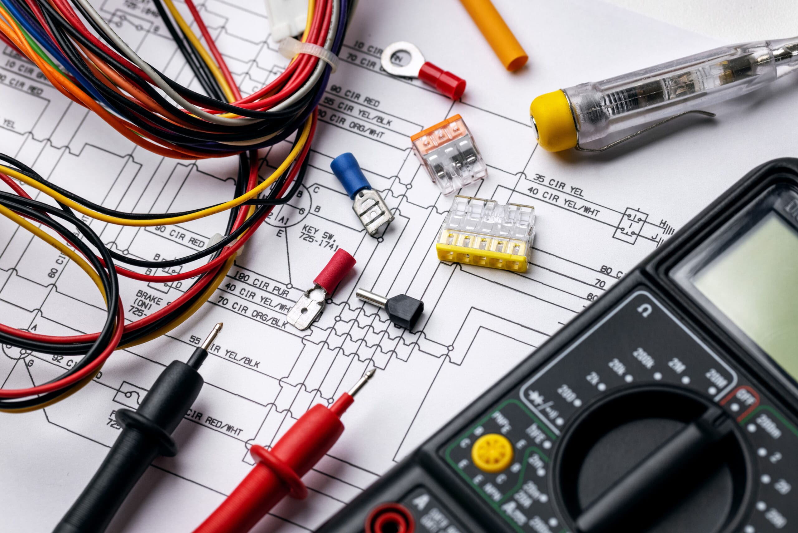 Assorted electrical tools, wires, circuit fuses, and a multimeter placed on an electronic schematic diagram, suggesting electrician testing, rewires, or repair work.