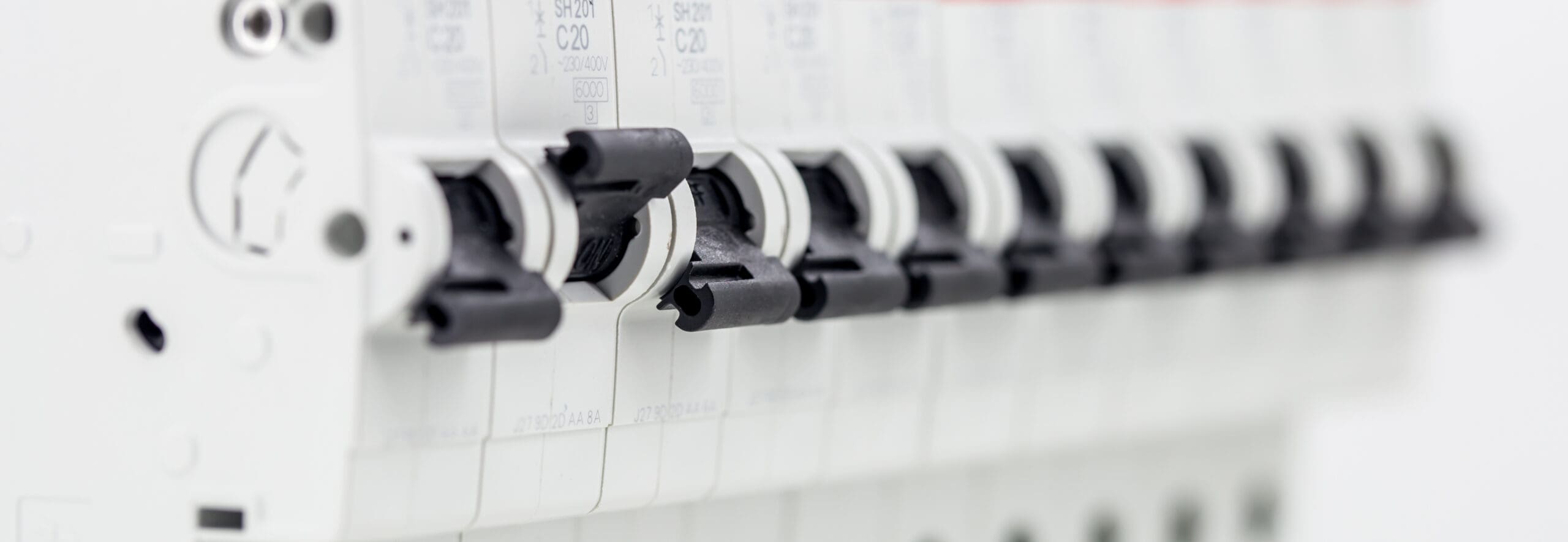 Close-up view of a row of black electrical circuit breaker switches installed on a white panel, commonly seen in Solar PV Installations, aligned in a neat line with soft focus on the background.